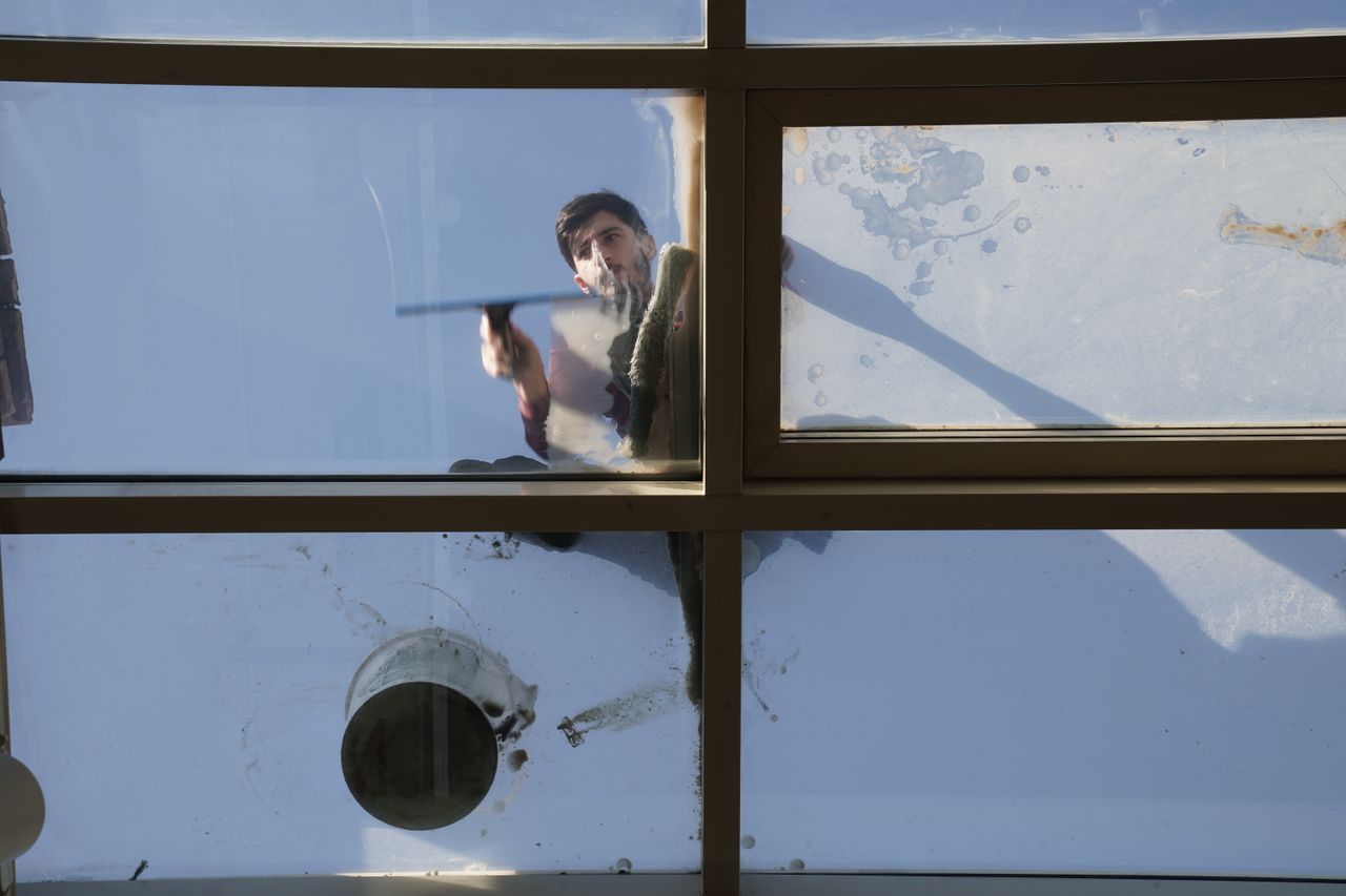 journey-01 A man cleaning the outside glass roof from above with a tool in daylight.
